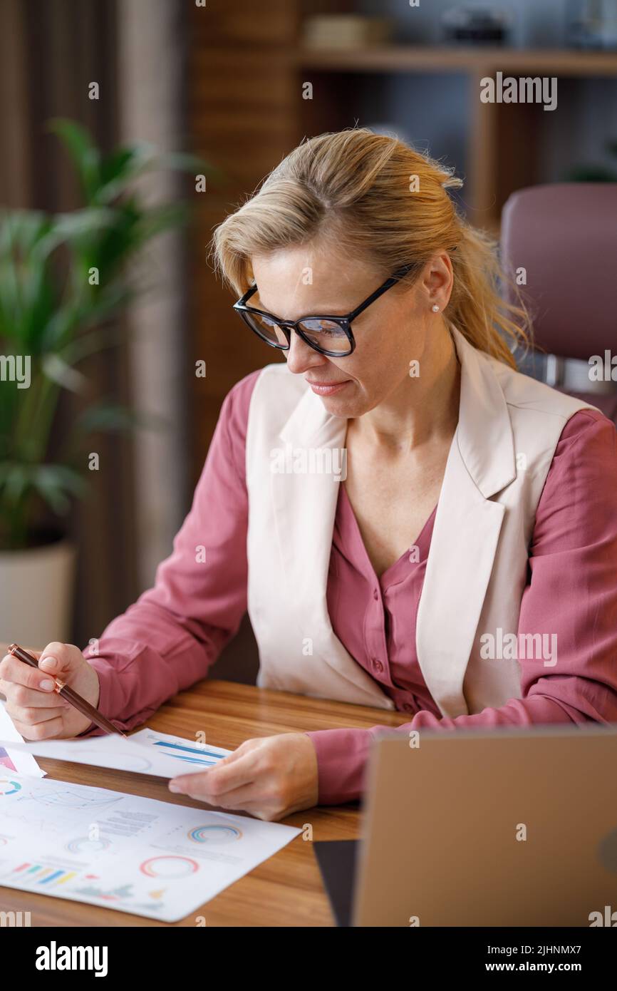 Retrato de una mujer de negocios adulta con gafas trabajando en la oficina. Gerente mujer haciendo papeleo, analizando informe financiero, sosteniendo documentos Foto de stock