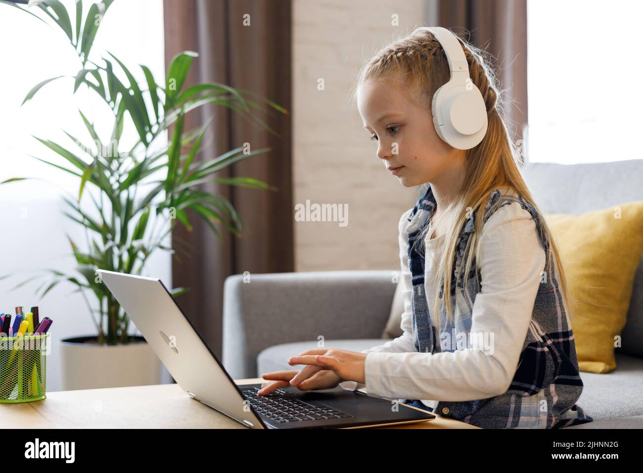 Linda niña de escuela primaria estudiando en casa usando una computadora portátil. Niño serio haciendo la tarea, contestando la pregunta en línea de la prueba, pasando el examen Foto de stock