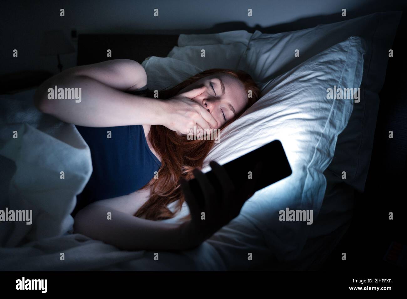 Mujer usando un smartphone en la cama tarde por la noche en la cama Foto de stock
