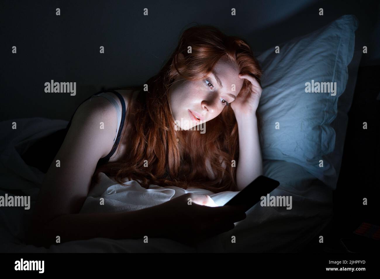 Una mujer sosteniendo el teléfono móvil en la cama tarde por la noche Foto de stock