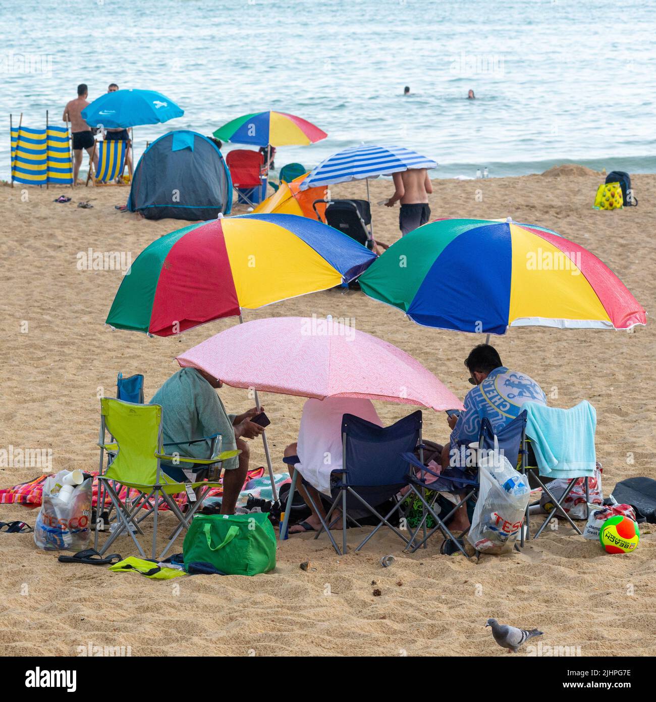 Boscombe, Bournemouth, Dorset, Inglaterra, Reino Unido, 19th Julio 2022, Tiempo. La gente que se sienta en la playa usa las sombrillas como sombrillas en la ducha de olas de calor. Foto de stock