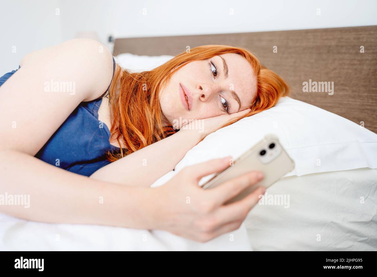 Mujer sosteniendo el teléfono móvil y acostada en la cama Foto de stock