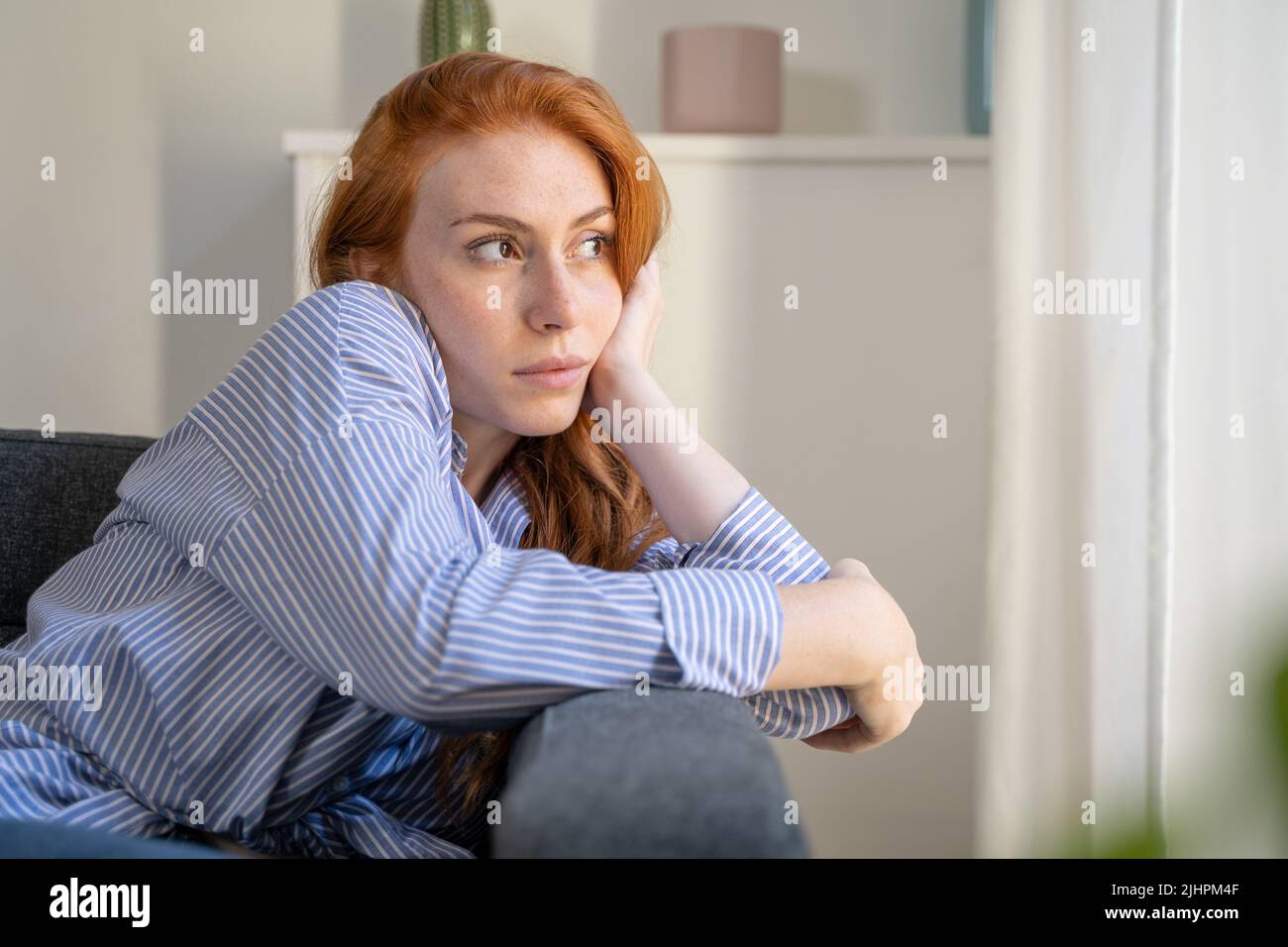 Mujer deprimida sentada en el sofá en casa, pensando en las cosas de la vida Foto de stock