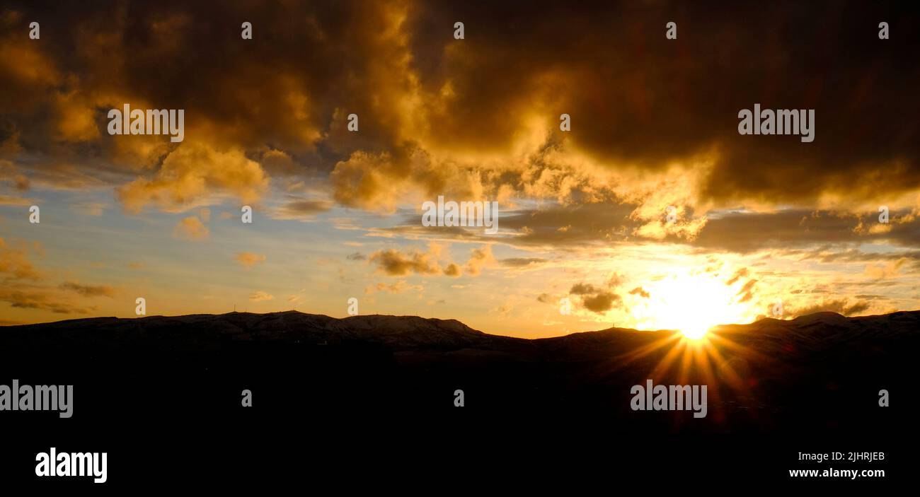 Puesta de sol sobre las montañas horizonte nubes sunstar sun star brillante brillante Foto de stock