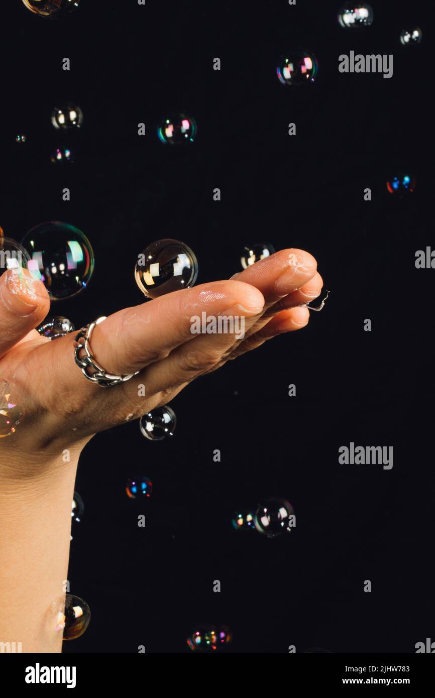 mujer que sostiene la mano aplanada haciendo gestos con burbujas flotantes y tocables sobre fondo negro Foto de stock