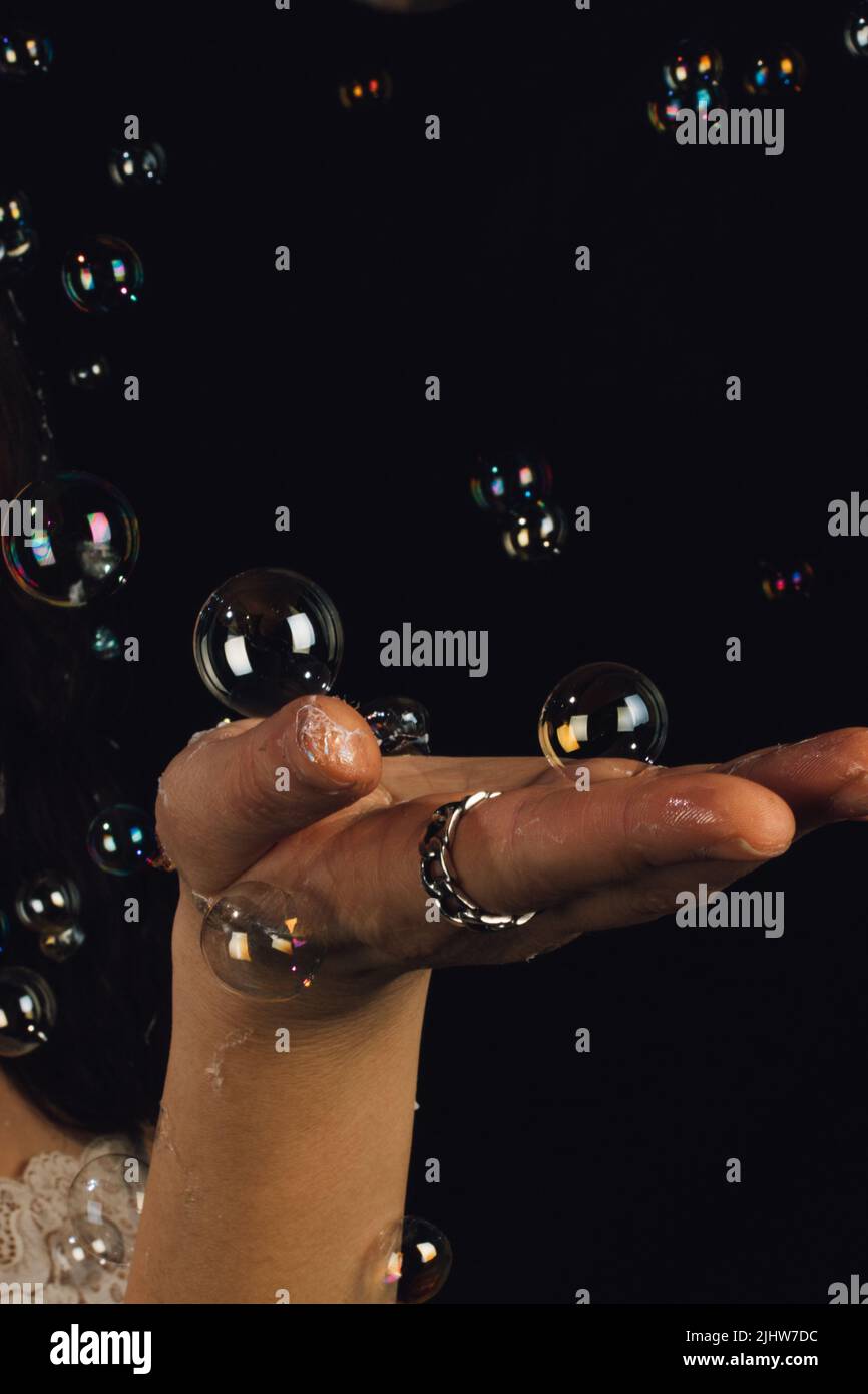 mujer que sostiene la mano aplanada haciendo gestos con burbujas flotantes y tocables sobre fondo negro Foto de stock