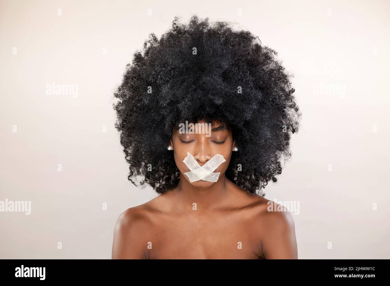 Modelo femenino afroamericano tranquilo con peinado afro y cinta en los labios de pie con ojos cerrados sobre fondo blanco en el estudio Foto de stock