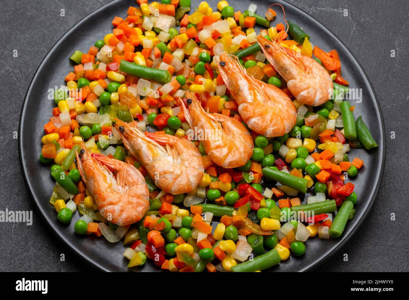 Gambas con verduras mixtas y espárragos verdes sobre plato negro. Vista superior. Fondo negro Foto de stock