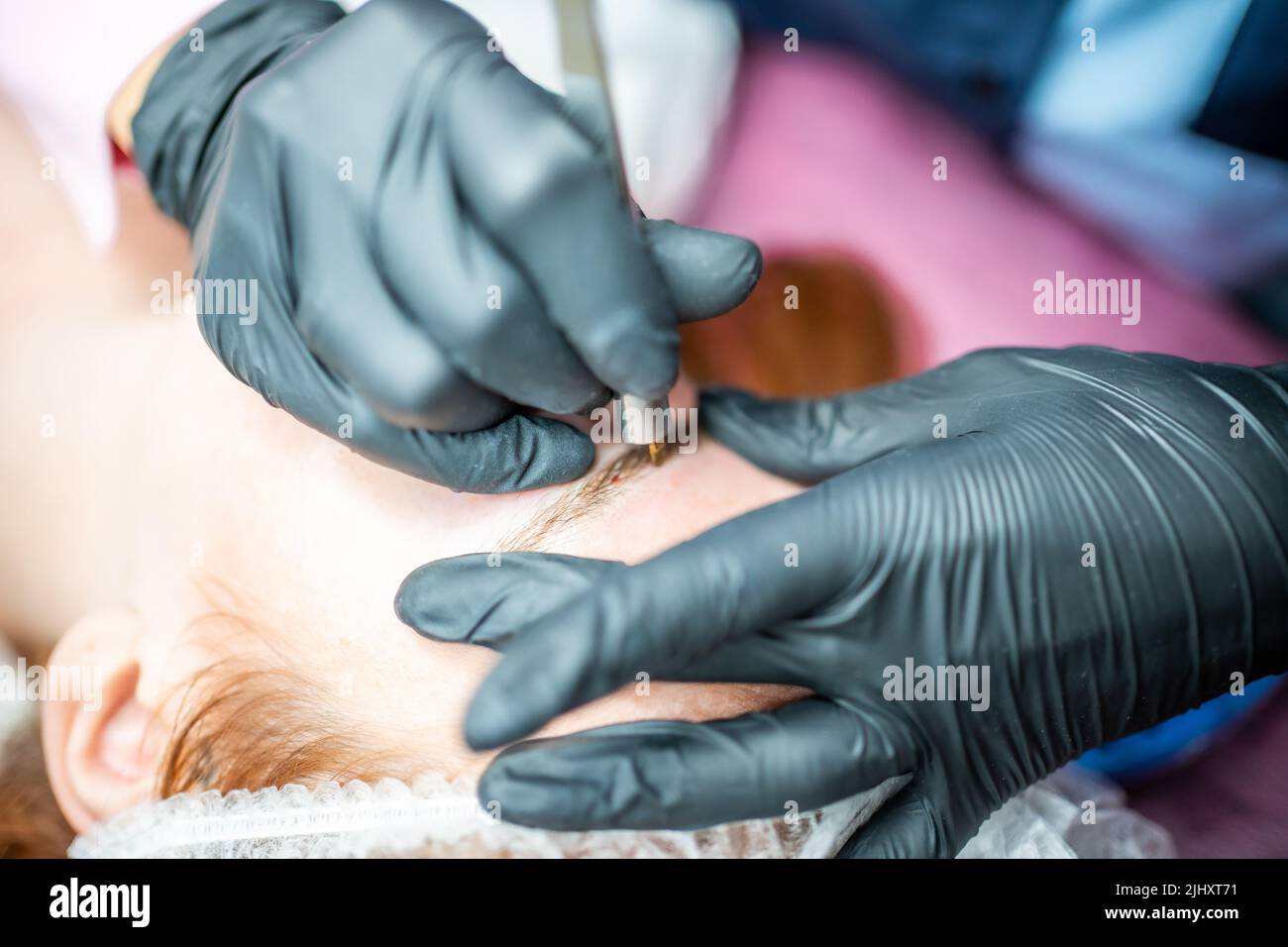 Procedimiento de microblading de cejas. Un maestro en guantes negros está haciendo una aguja de mezcla de la ceja de modelo. Foto de stock