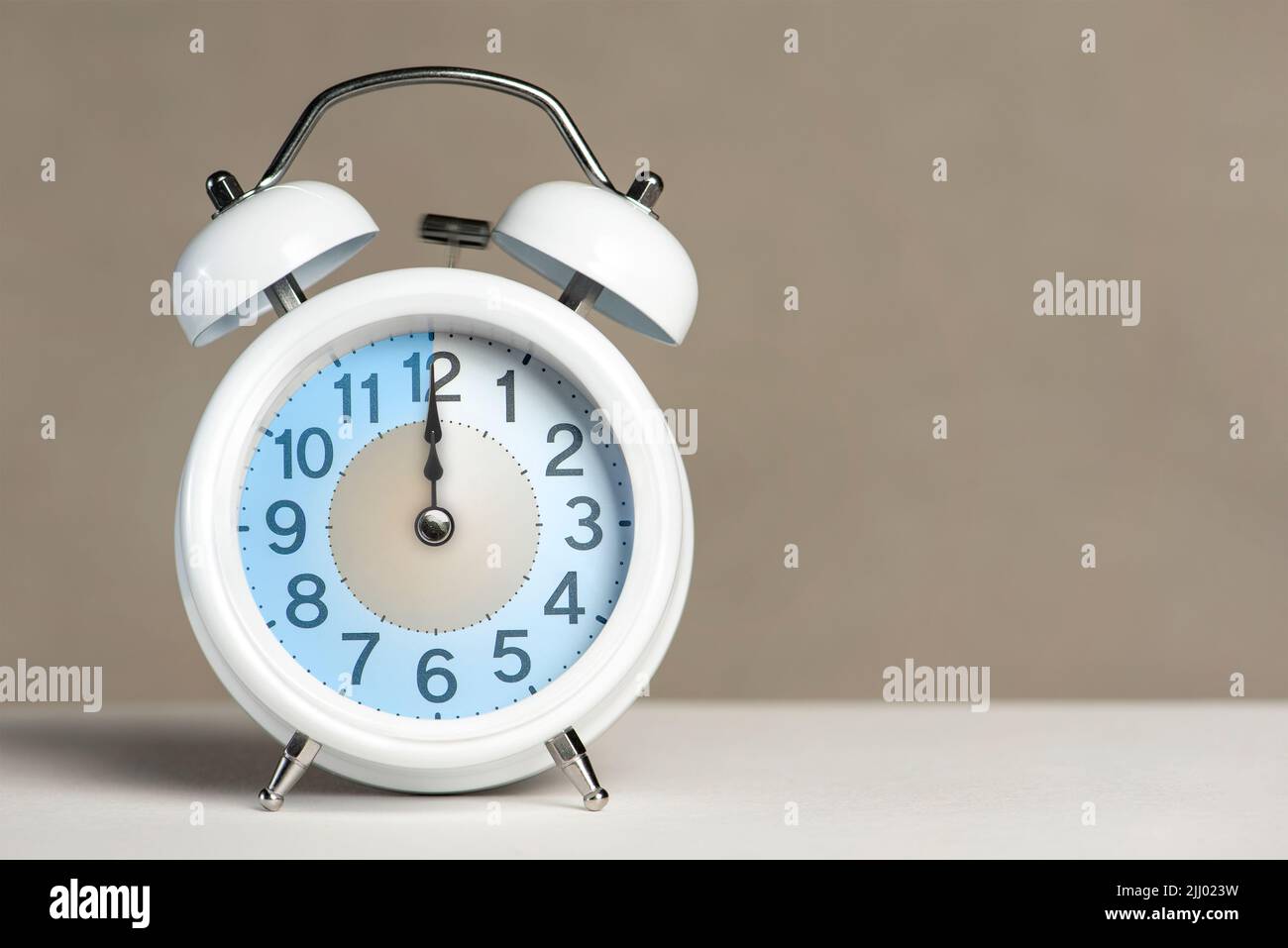 Doce en punto en la alarma. Un despertador blanco está sobre una mesa  blanca. La manecilla del reloj apunta a las 12 en punto. Tiempo para  cambiar a horario de verano o