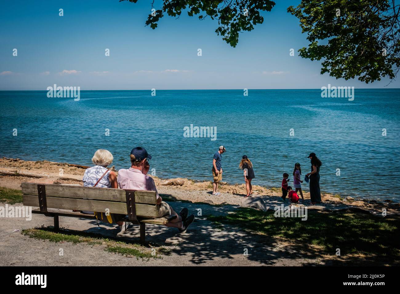 Una pareja de ancianos mirando a estos niños y grandes niños juegan junto al agua en un caluroso día de verano Foto de stock