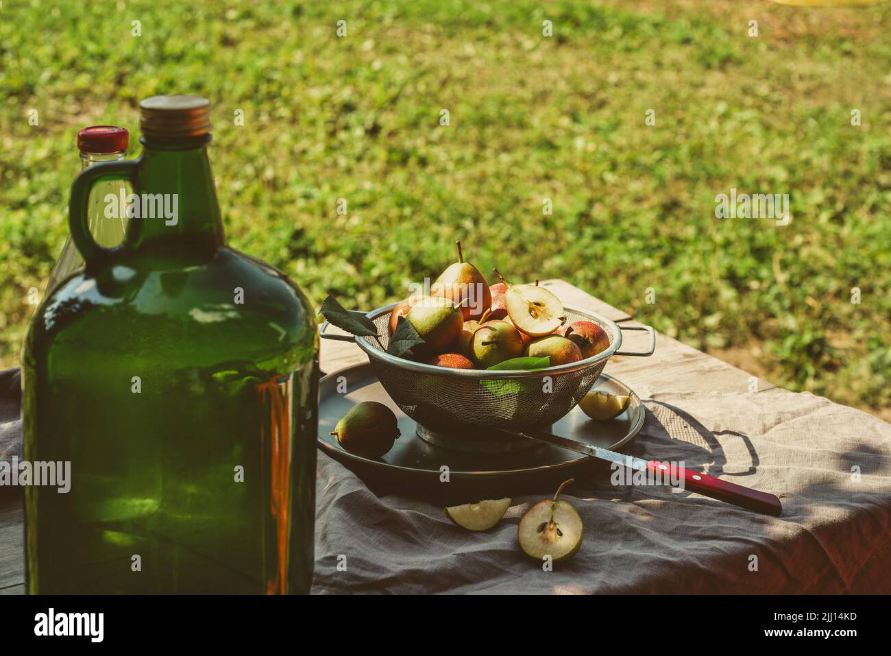 Una botella grande de sidra de fruta sobre mesa rústica con cosecha de peras, en un día de otoño Foto de stock