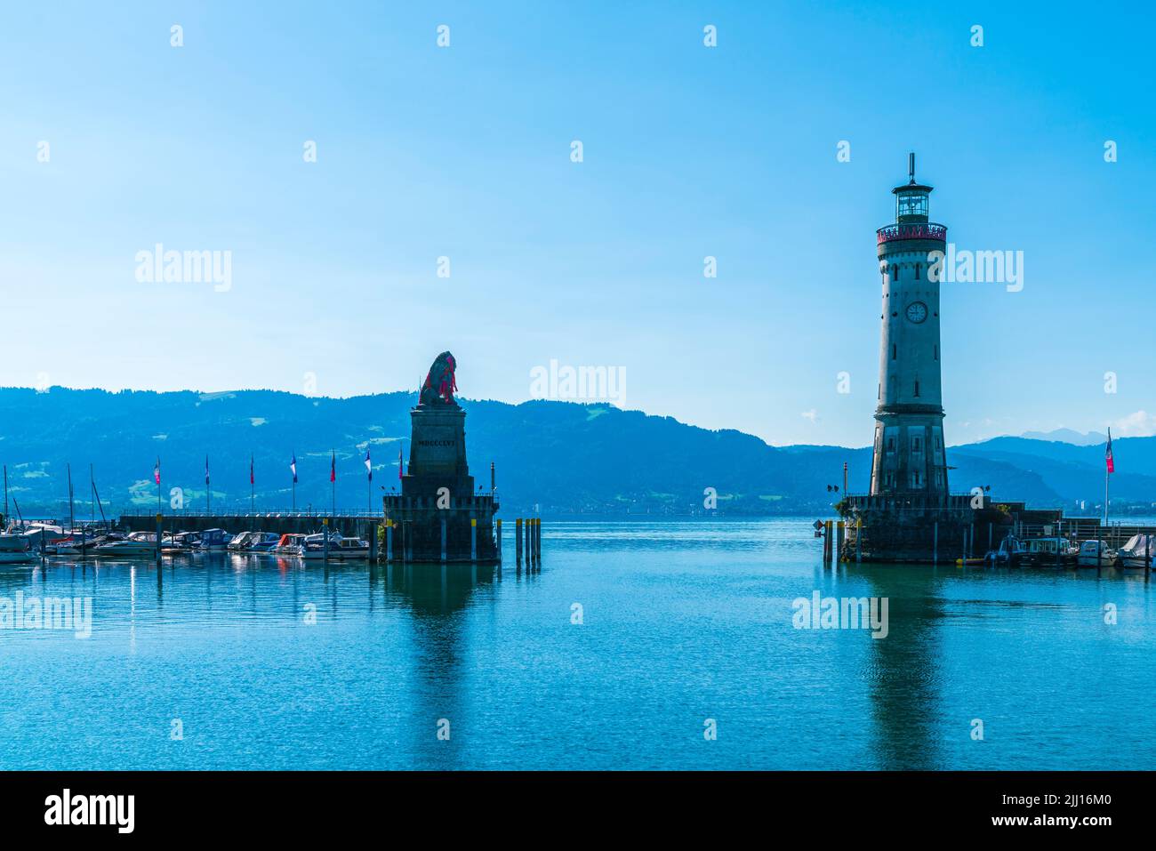 Alemania, el faro del puerto de la ciudad de la isla de Lindau con vistas a austria y la ciudad de bregenz temprano en la mañana con cielo azul y sol en verano Foto de stock