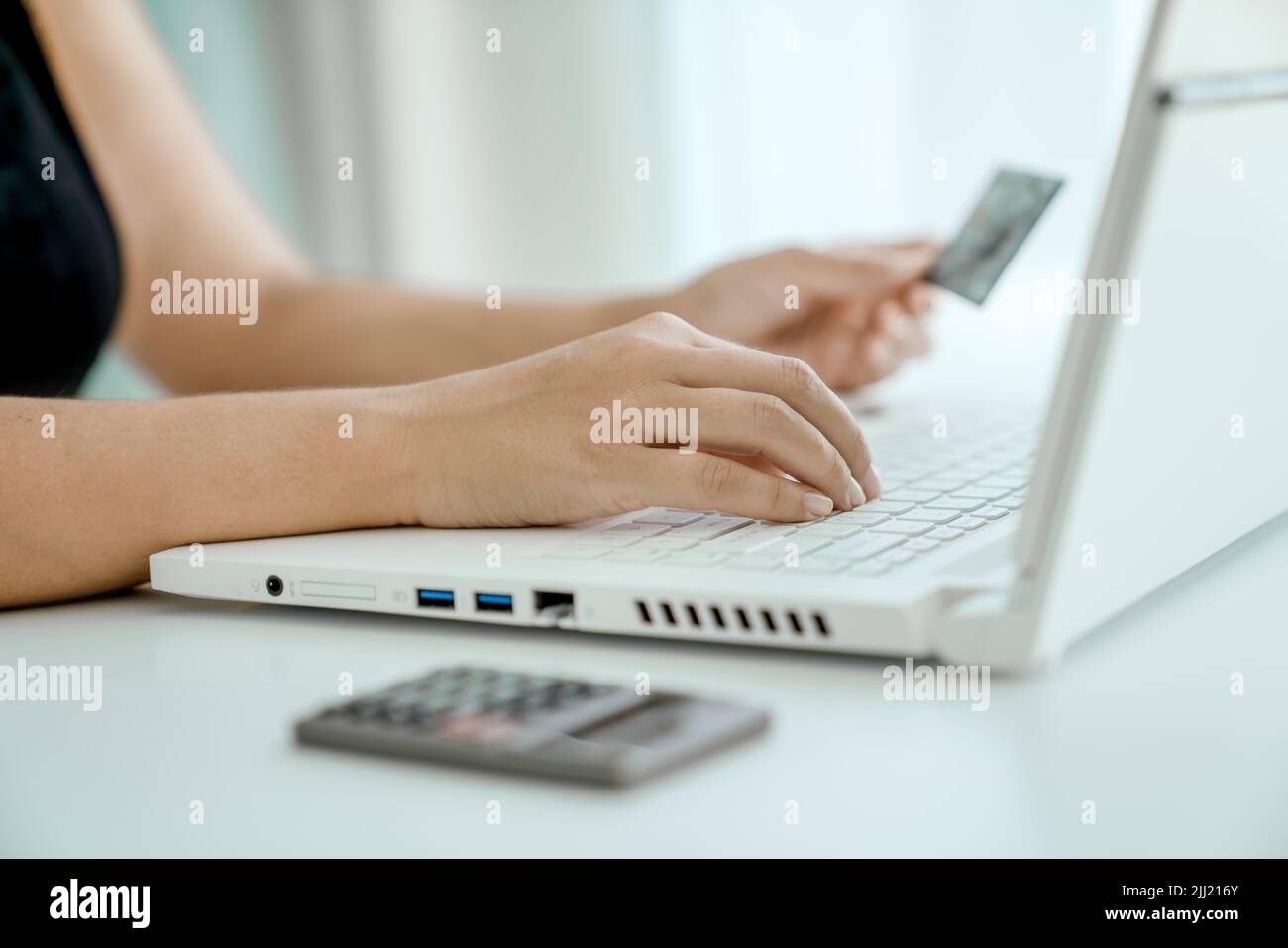 Mujer hace compras en línea sentado frente al ordenador portátil con la tarjeta bancaria en la mano. Manos en primer plano. Concepto de compras en línea y transferencia de dinero. Foto de stock