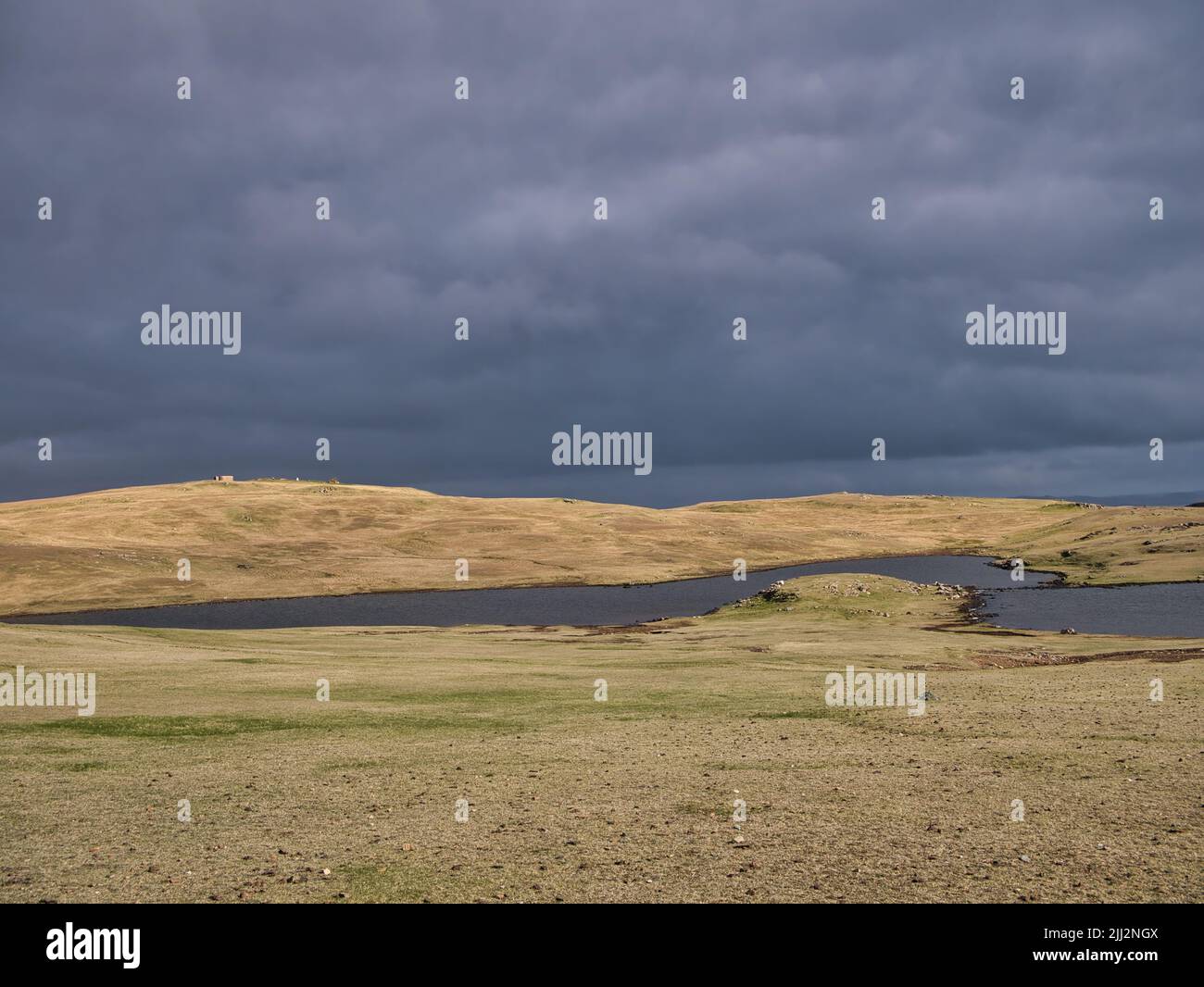Antes de la lluvia, nubes oscuras sobre un paisaje sin árboles y lochen (lago pequeño) en Eshaness, Shetland, Reino Unido. Foto de stock