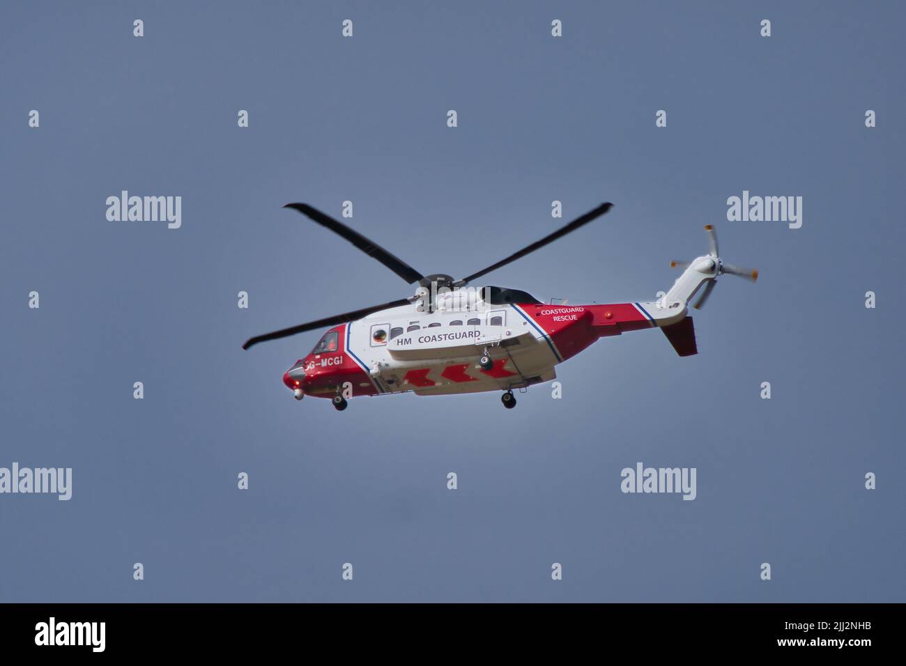 Un helicóptero Sikorsky S-92A, rojo y blanco, del guardacostas HM, en vuelo contra un cielo gris azul. Foto de stock