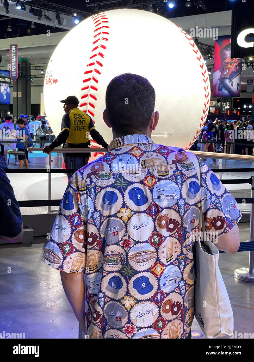 Un fan en el Play Ball Fest que acompaña al All-Star Game lleva una camisa hawaiana con temática de los Dodgers de Brooklyn frente a un gigante de béisbol. Foto de stock
