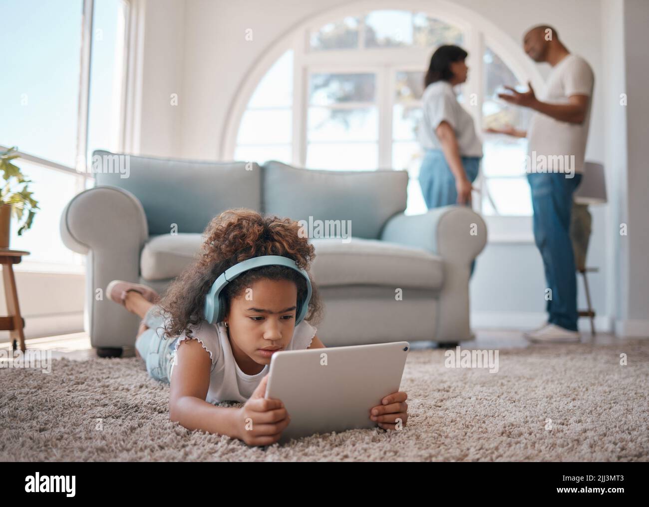 Luchar alrededor de los niños nunca está bien. Una niña que usa una tableta digital mientras sus padres discuten. Foto de stock