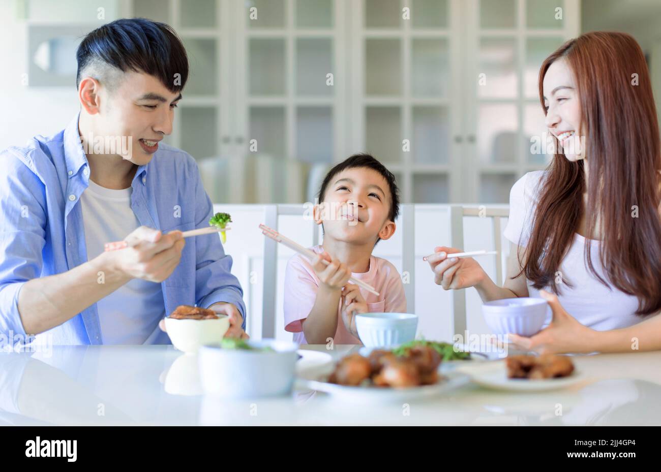 el niño disfruta comiendo con su padre y su madre. Feliz familia asiática cenando en casa Foto de stock