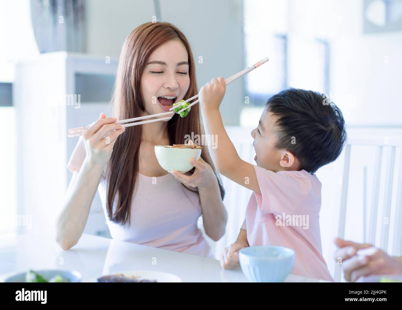 a niño pequeño le gusta comer con la madre. Feliz familia asiática cenando en casa Foto de stock