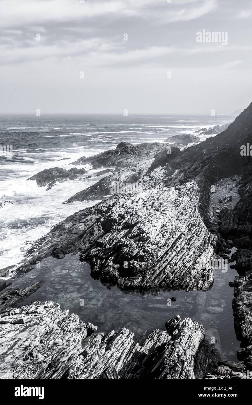 Contemple una piscina de aguas aisladas a lo largo de la rocosa costa Tsitsikamma, en la Garden Route Sudáfrica en blanco y negro Foto de stock