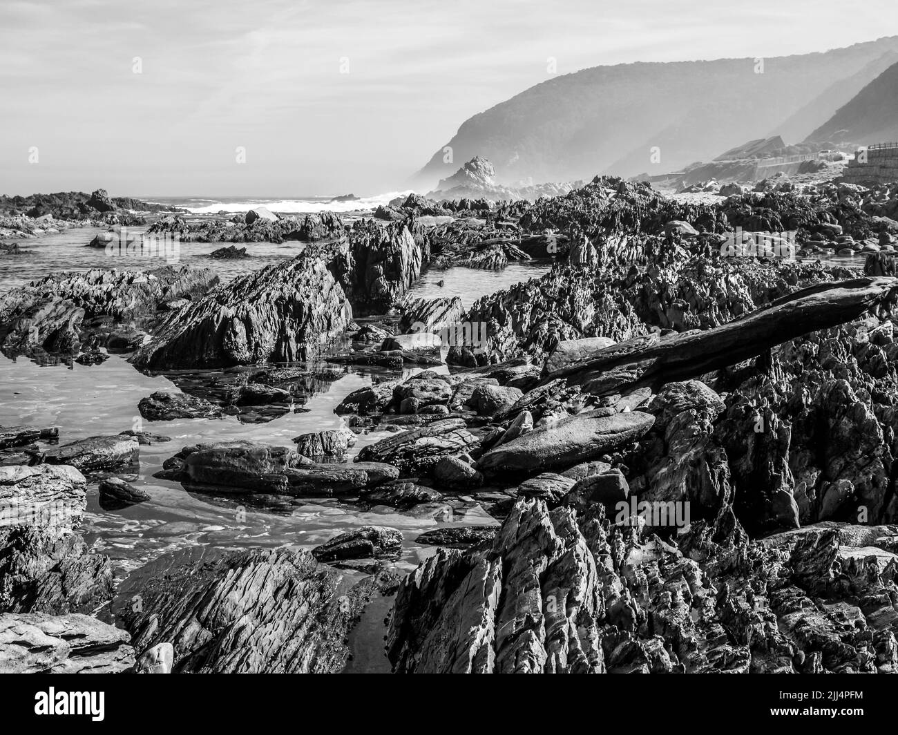 La escarpada costa rocosa a lo largo de la costa sur de Sudáfrica, con las montañas Tsitsikamma elevándose en el fondo. Foto de stock