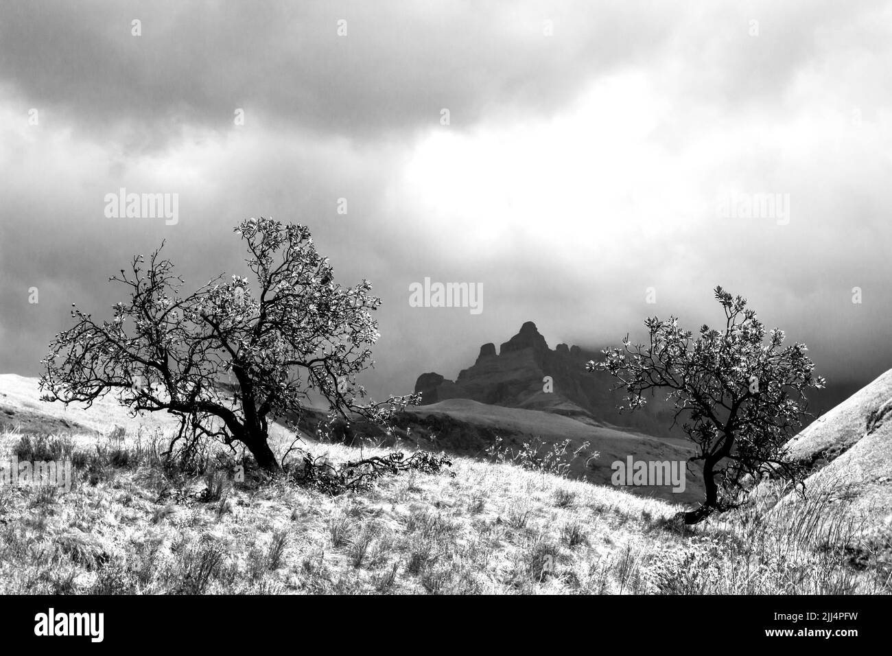 Vista ominosa en blanco y negro de una tormenta que se reúne alrededor de los altos picos de las montañas Drakensberg de Sudáfrica Foto de stock