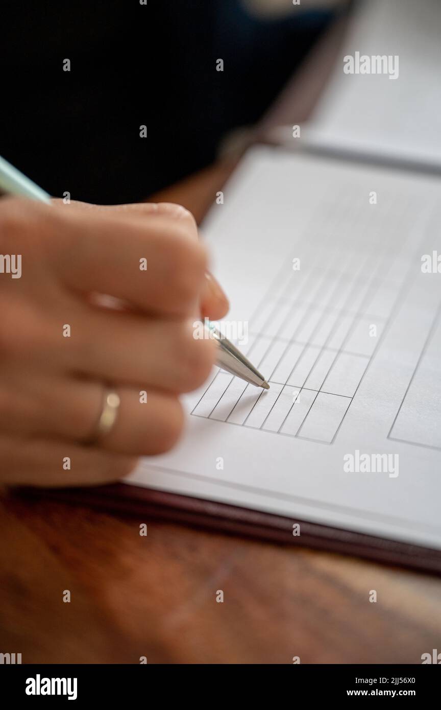Vista de primer plano de una mujer de negocios rellenando los datos en una tabla impresa en papel blanco. Foto de stock