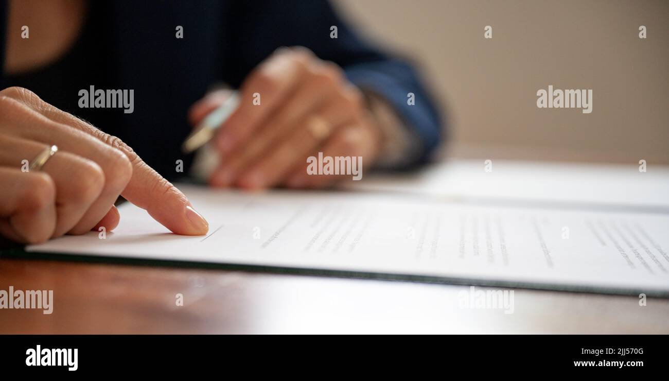 Vista de primer plano de ángulo bajo del empresario o abogado que señala una línea de firma en la parte inferior del documento legal o contrato. Foto de stock