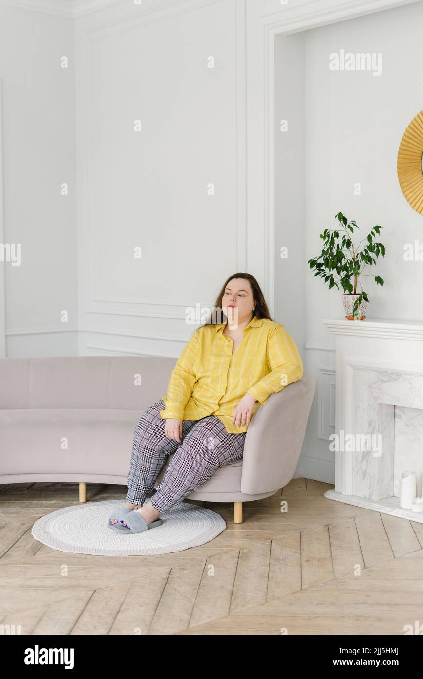 Pensativo mujer sentada en un sofá en casa Foto de stock