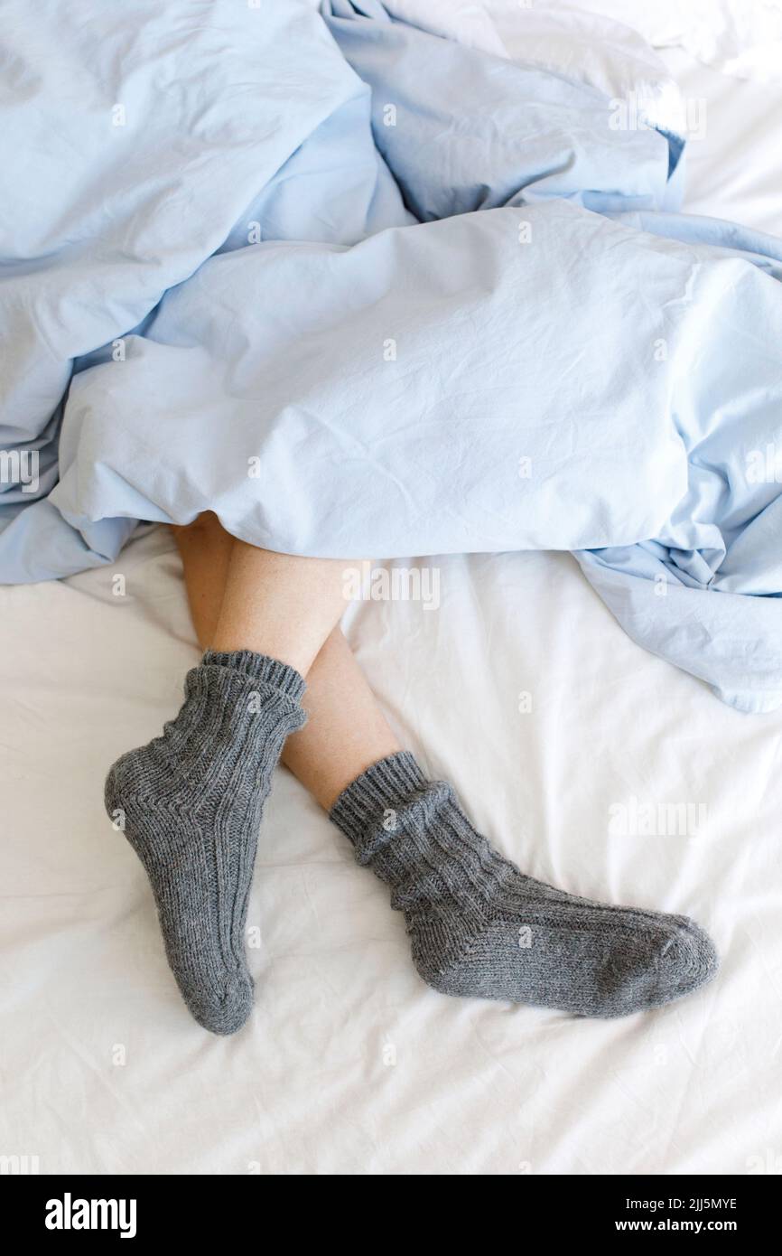 Piernas de mujer con calcetines abrigados bajo manta en la cama Foto de stock