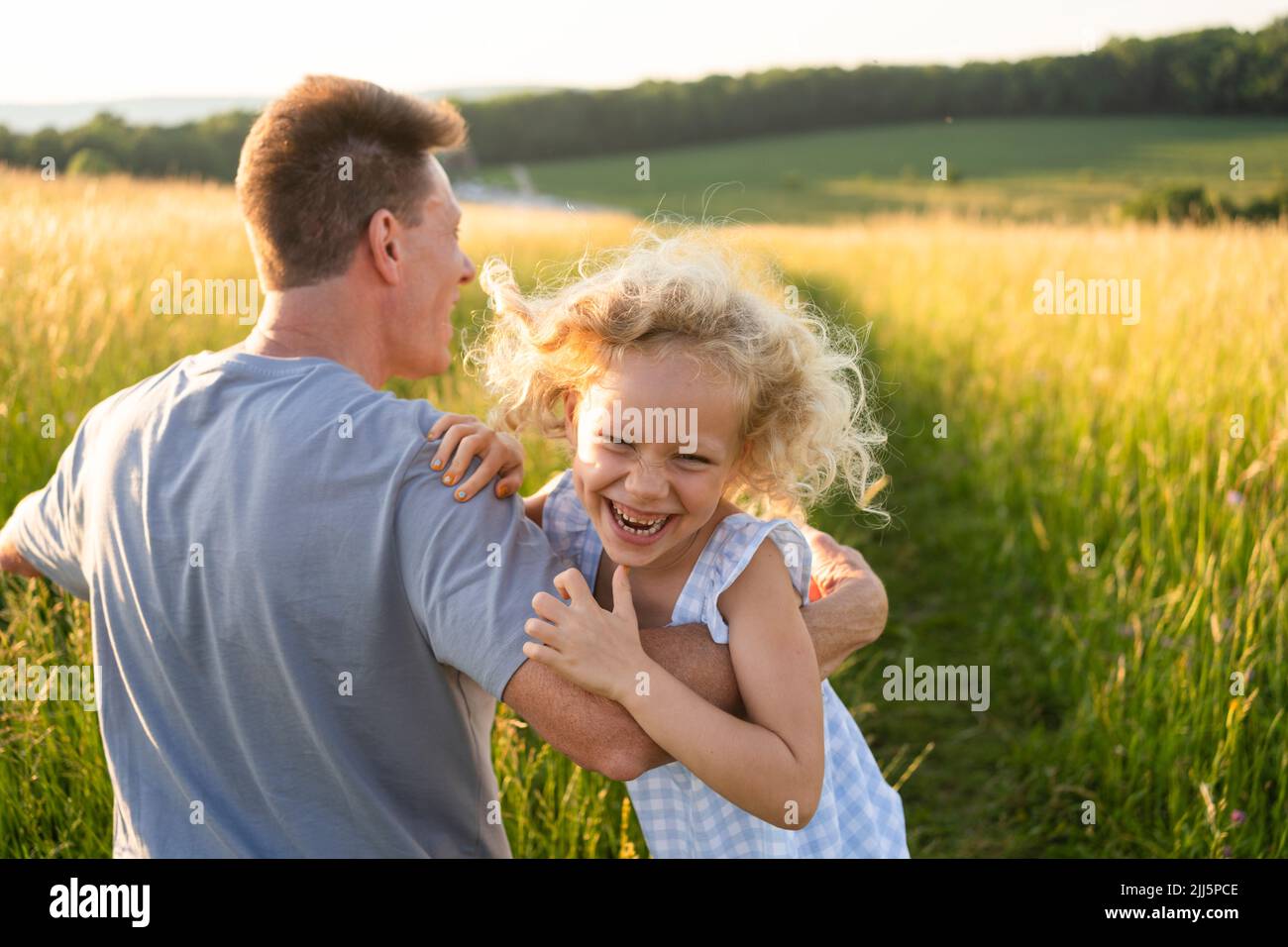 Juguetona chica rubia disfrutando con el padre en el campo Foto de stock