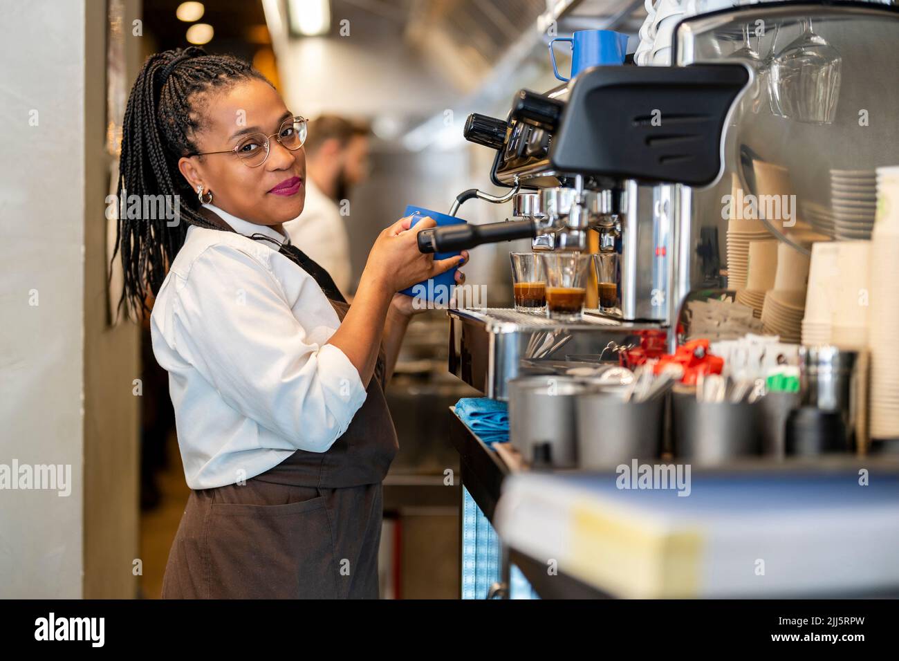 Barista sonriente con cafetera en la cocina del restaurante Foto de stock