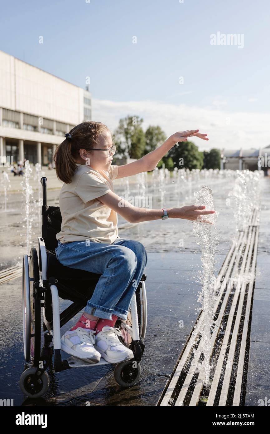 Chica en silla de ruedas jugando con una fuente en un día soleado Foto de stock