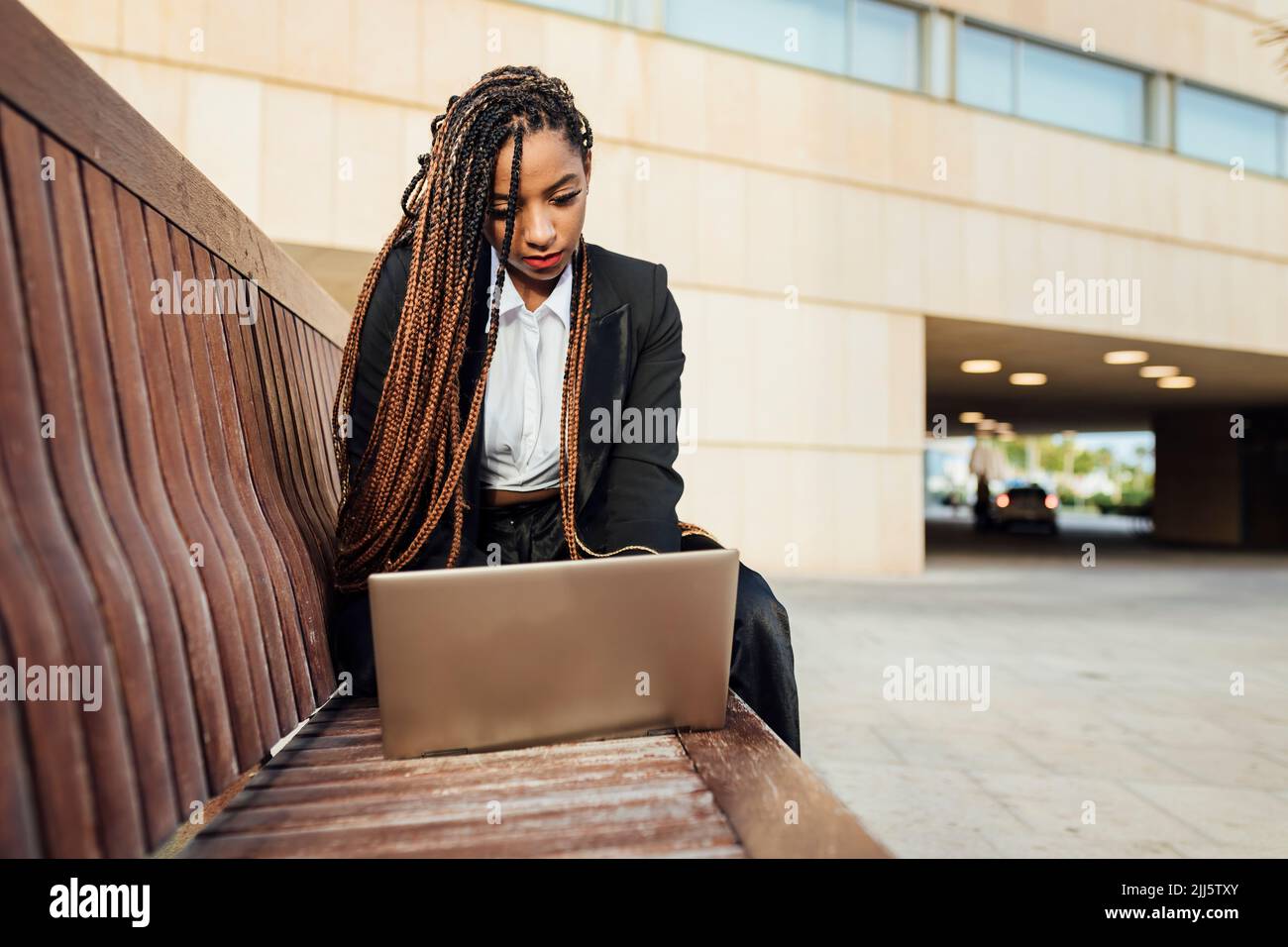 Mujer de negocios joven con un ordenador portátil sentado en un banco Foto de stock