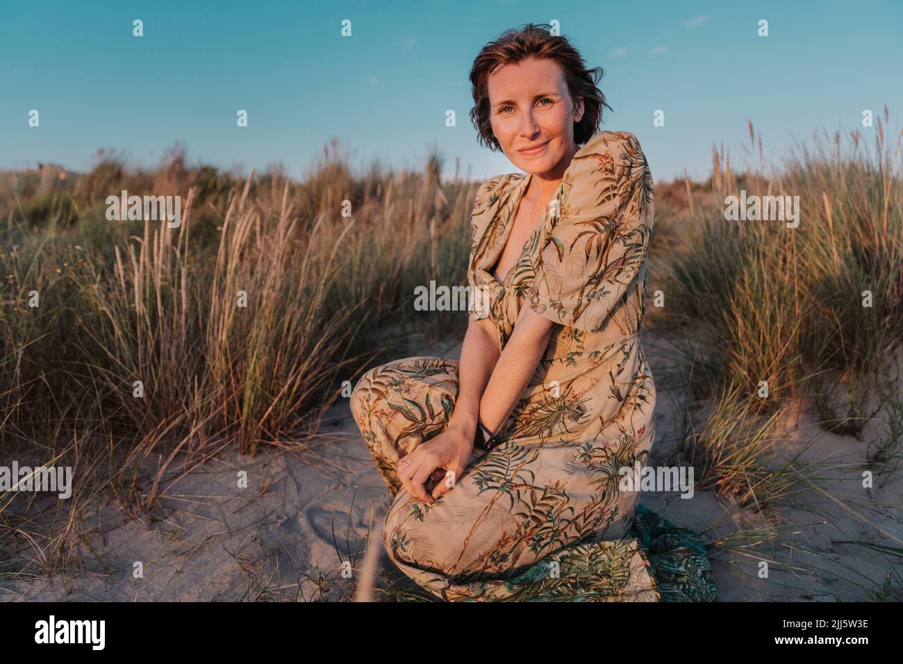 Mujer sonriente arrodillada por las plantas en la playa Foto de stock