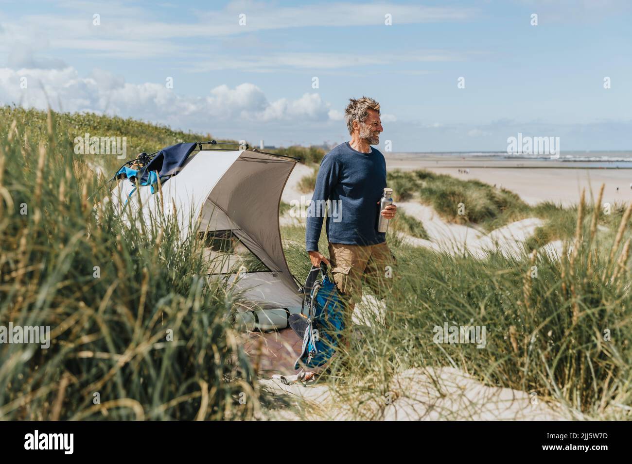 Hombre maduro feliz acampando en un día soleado en la playa Foto de stock