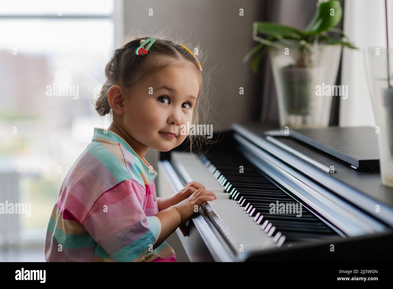 Niña linda tocando el piano en una escuela de música. Un niño preescolar  está aprendiendo a tocar un instrumento musical. Educación, concepto de  habilidades. La pequeña princesa es hap Fotografía de stock -