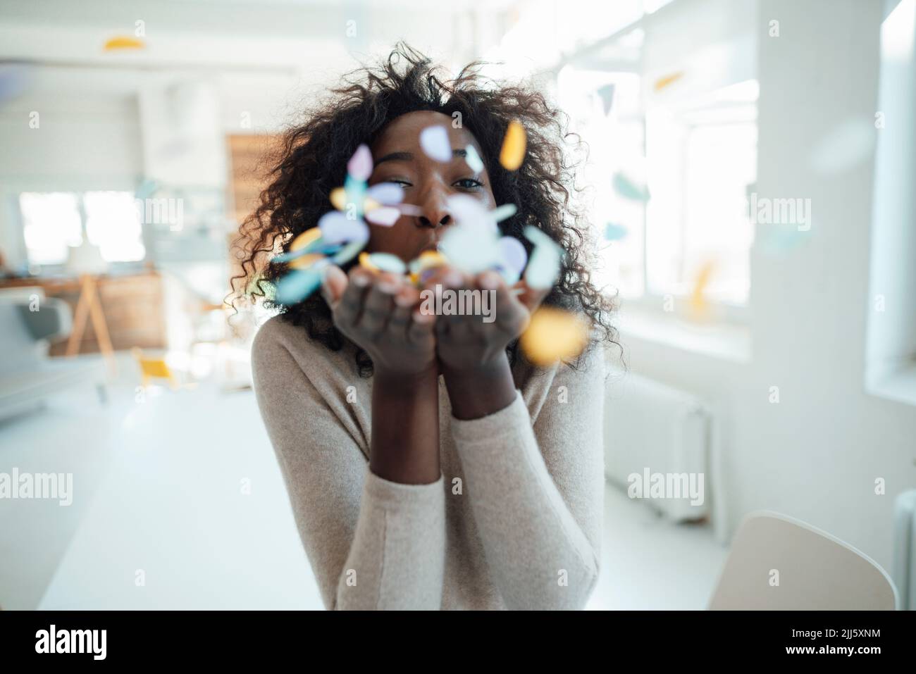Mujer joven con las manos ahuecadas soplando confeti Foto de stock