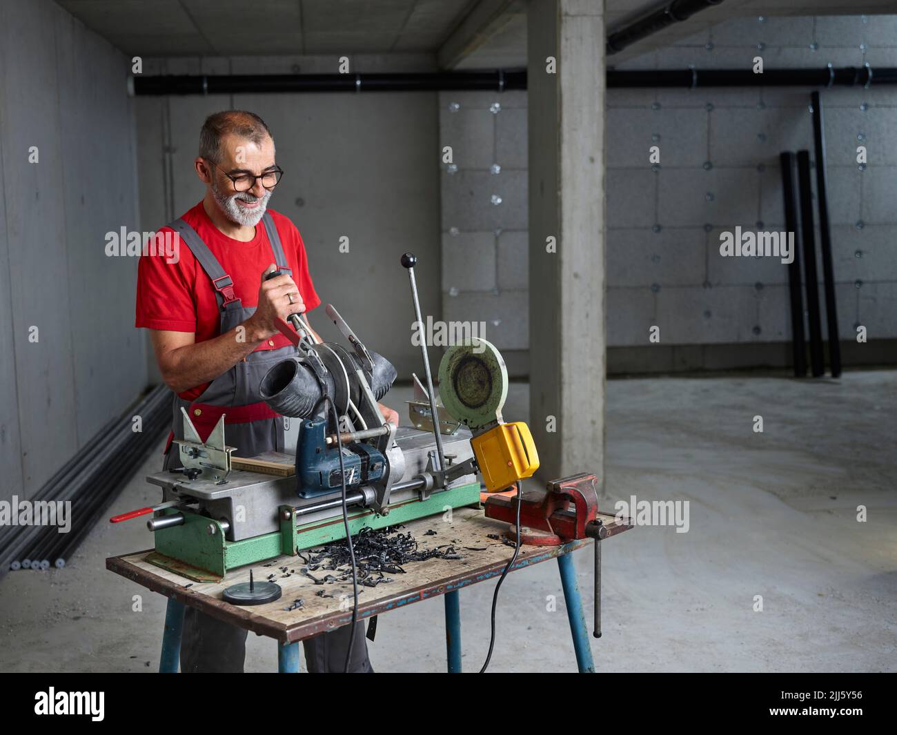 Sonriente fontanero usando gafas cortando tubería de plástico en el banco de trabajo Foto de stock