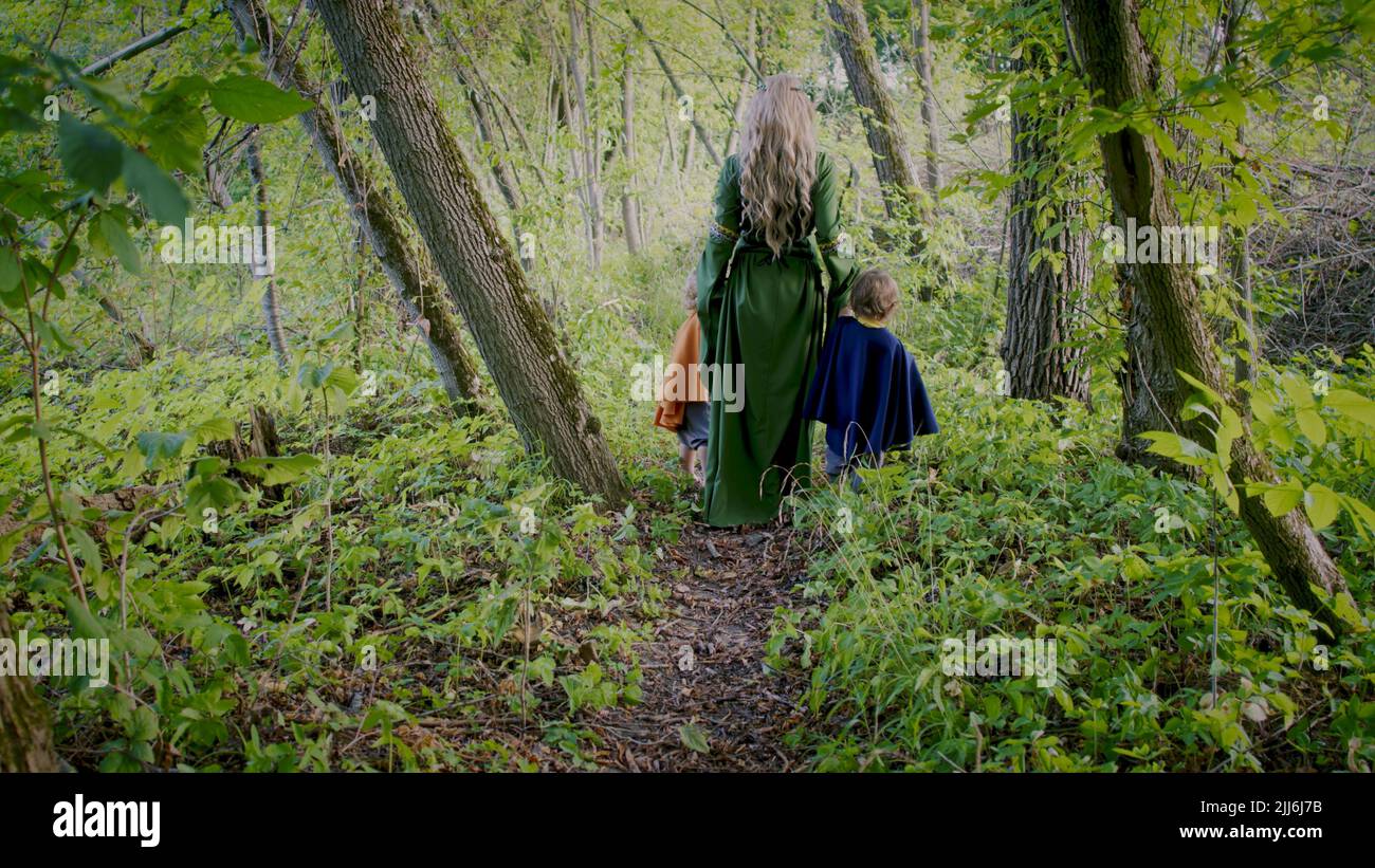 Dos niños pequeños cosplay gnomos o hobbits con la mujer elf caminar en el bosque verde. Personajes irreconocibles de cuento de hadas. Halloween, niños Foto de stock