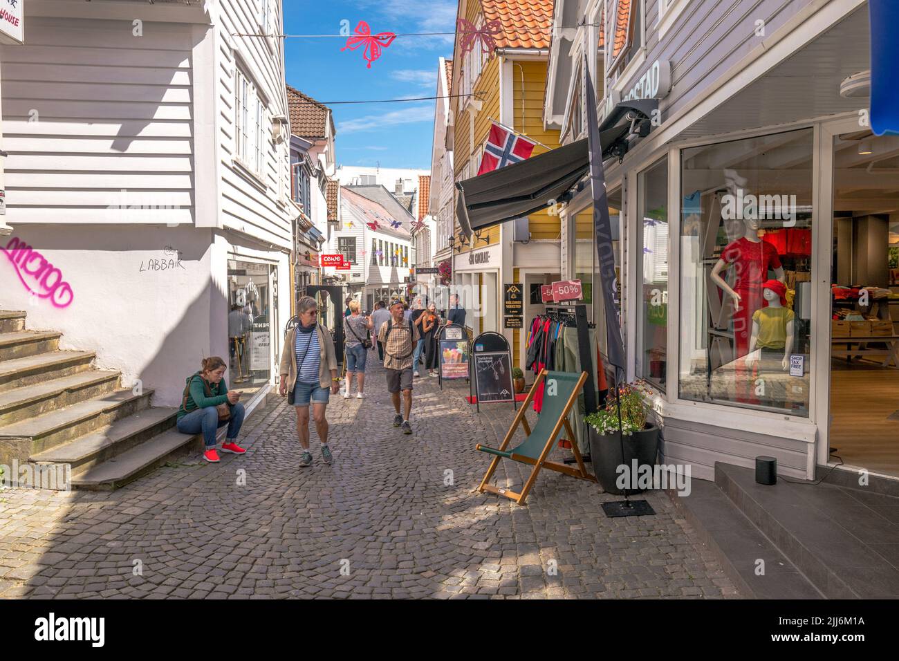 La gente camina a lo largo de la estrecha calle comercial adoquinada y los tradicionales edificios de madera en la ciudad de Savanger, Noruega. Foto de stock