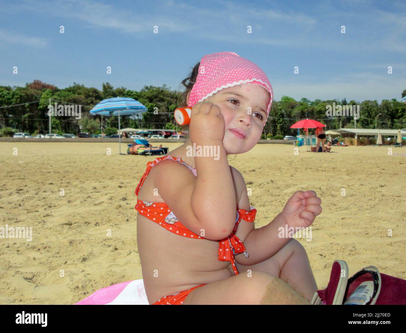 Imagen de una adorable niña sentada en la playa poniéndose protector solar. Protección de la piel para los niños en el mar Foto de stock