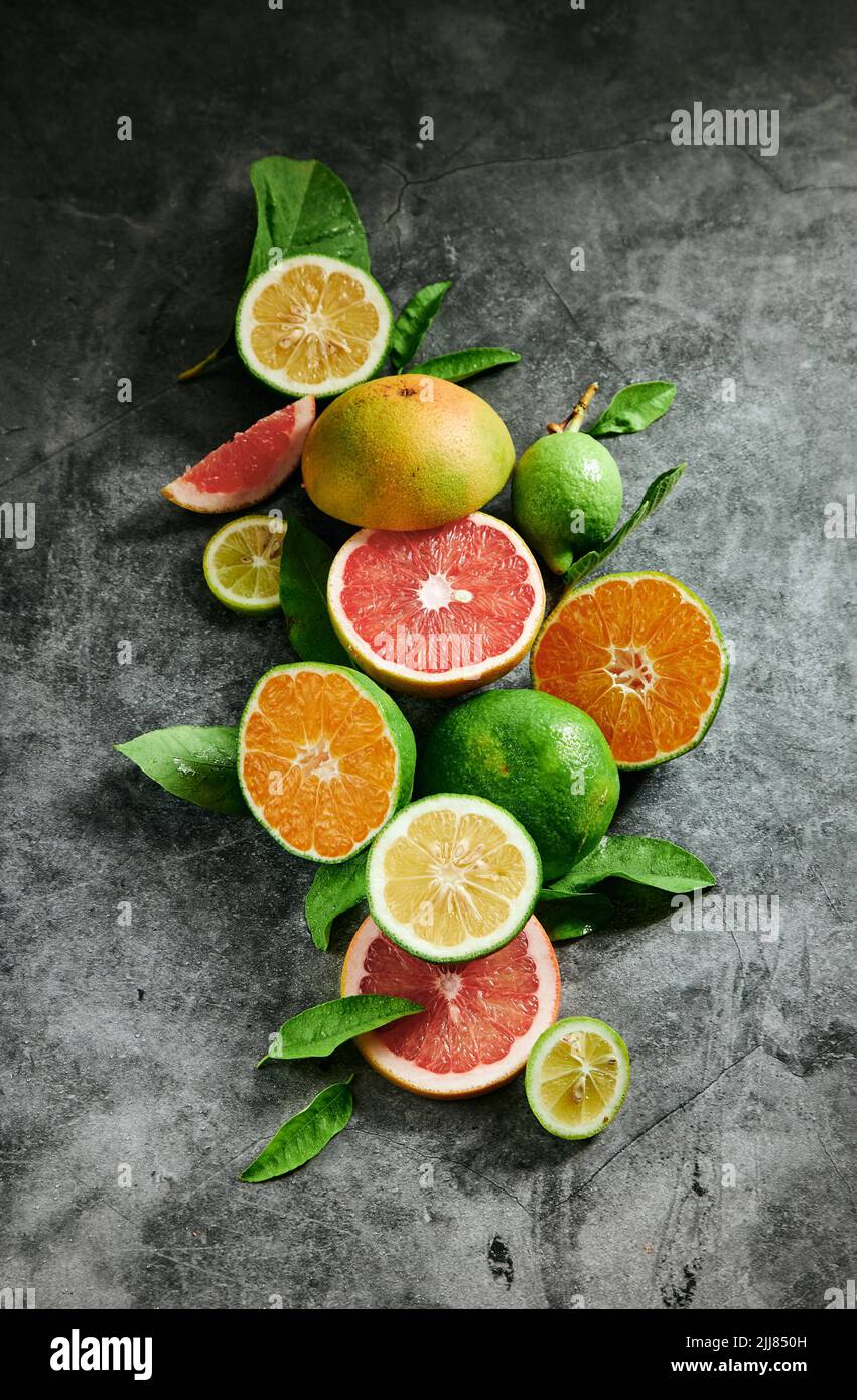 Desde arriba montón de frutas cítricas exóticas maduras y coloridas colocadas sobre fondo gris con hojas verdes en un estudio luminoso moderno Foto de stock