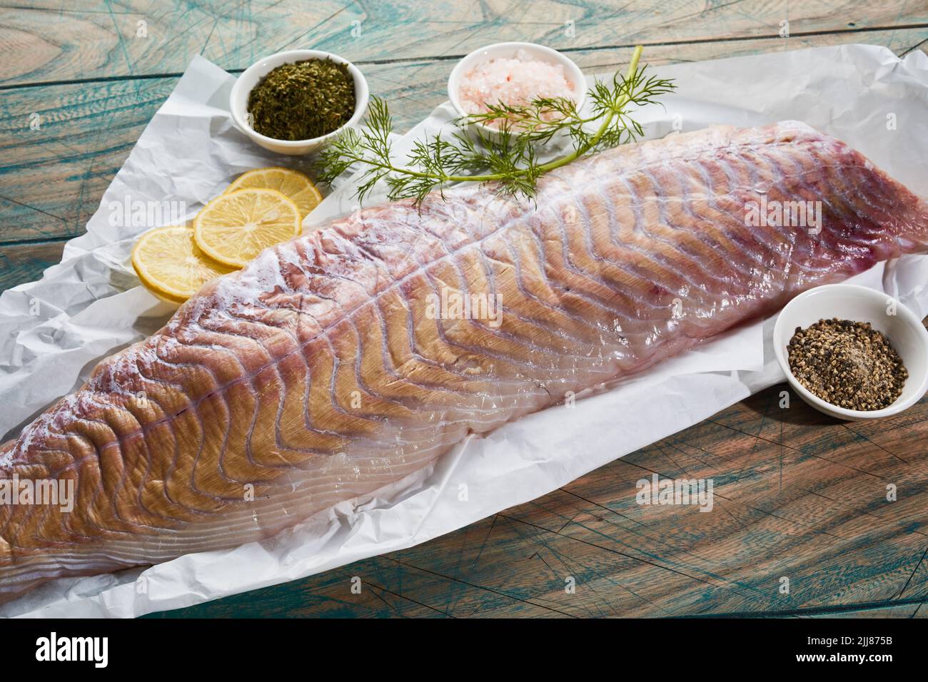 Gran ángulo de filete de pescado crudo colocado con especias y rodajas de limón sobre una mesa de madera en la cocina Foto de stock