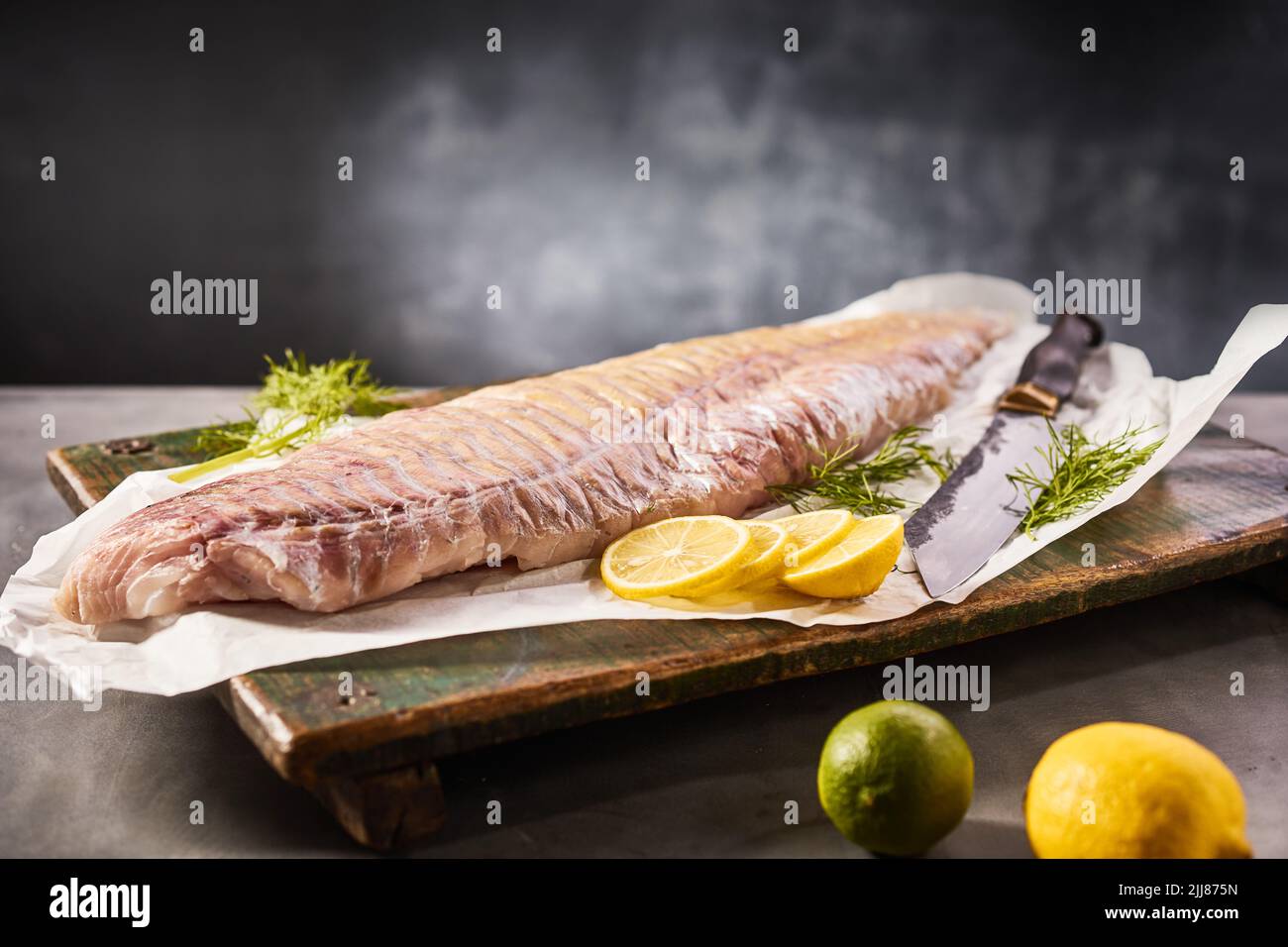 Filete de pescado fresco crudo con limón y eneldo colocado sobre una tabla de cortar de madera sobre una mesa en el estudio Foto de stock