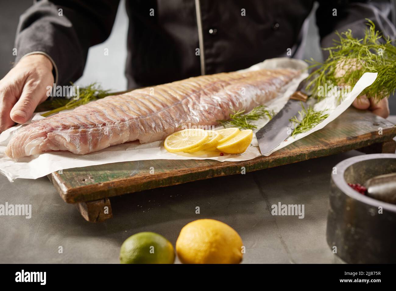 Crop anónimo chef masculino de pie con filete de pescado crudo en la tabla de cortar en la cocina Foto de stock