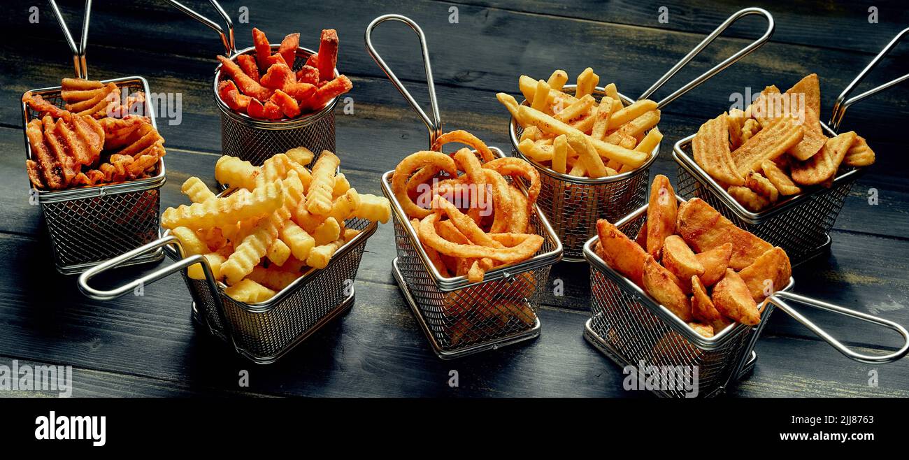 Gran ángulo de patatas fritas variadas y patatas fritas en cestas de metal dispuestas sobre una mesa de madera Foto de stock