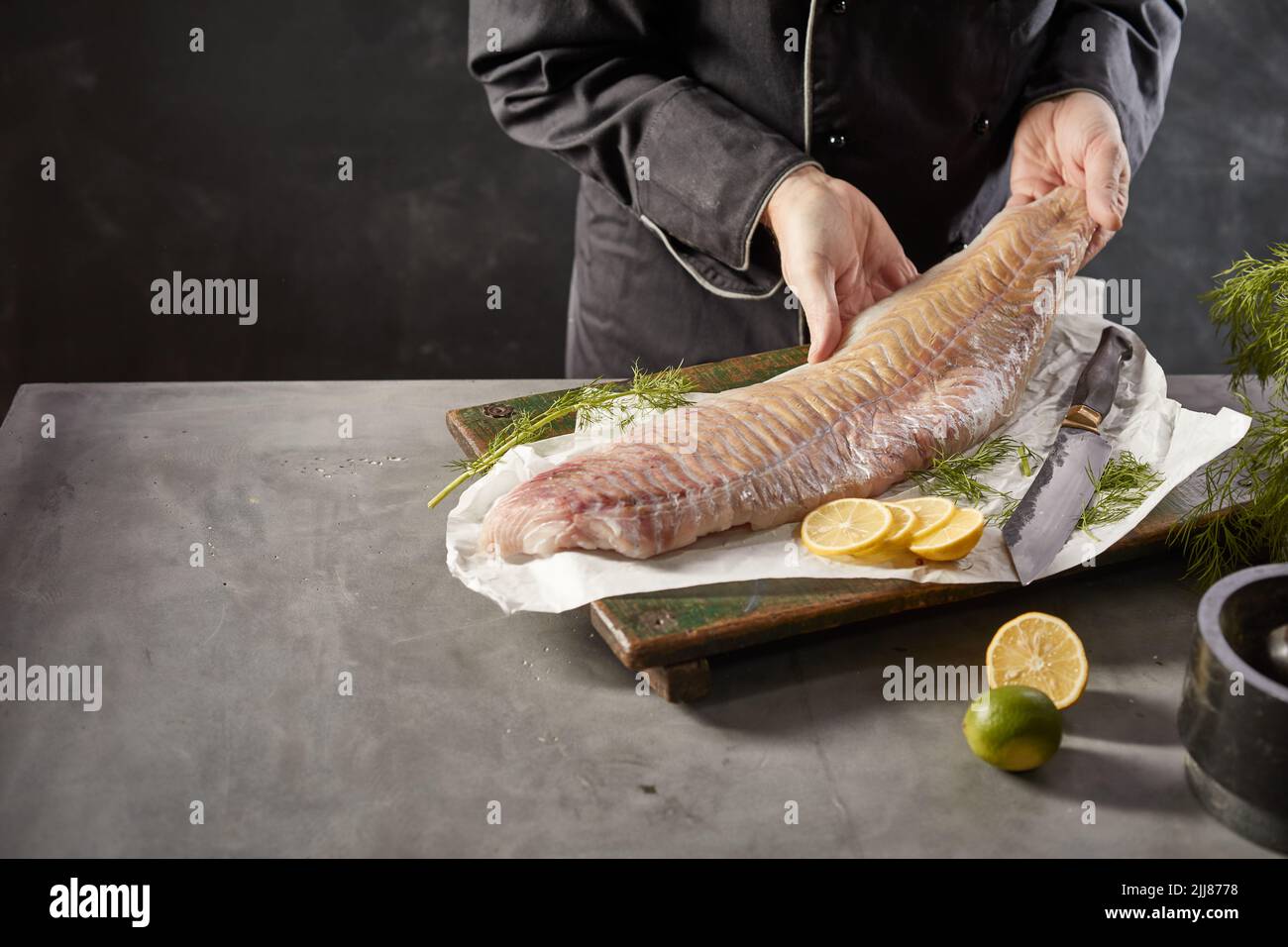 Alto ángulo de cultivo sin rostro macho cocinero de pie en la mesa con filete de pescado fresco crudo en la cocina Foto de stock