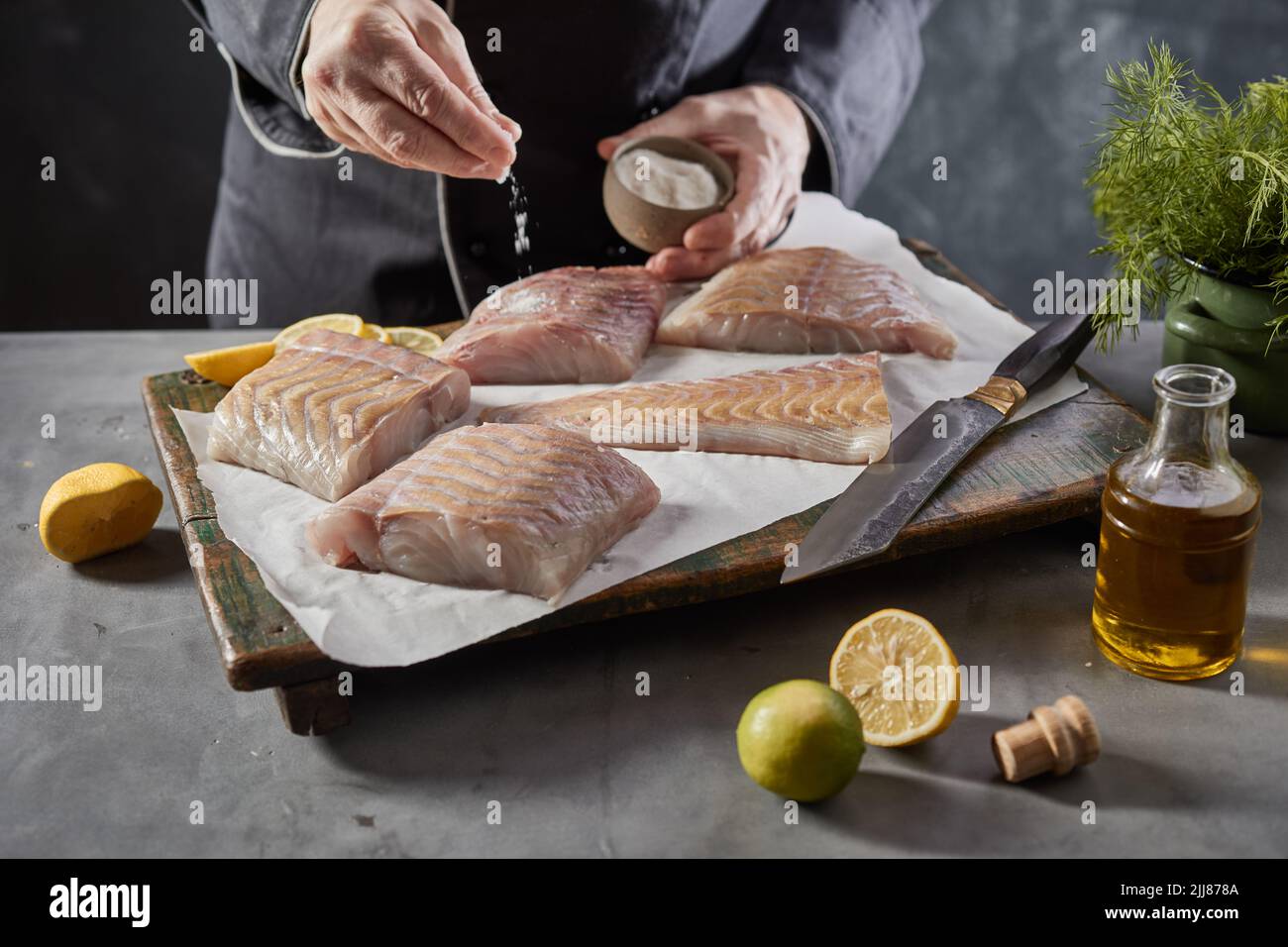 Ángulo alto de la cosecha irreconocible chef masculino vertiendo sal en rodajas de filete de pescado crudo mientras cocina en la cocina Foto de stock